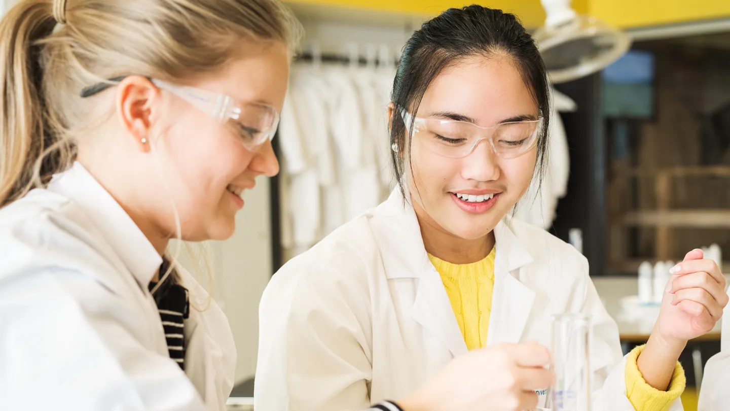 Två tonåringar klädda i glasögon och labbrock, experimenterar i Universeums kemilabb