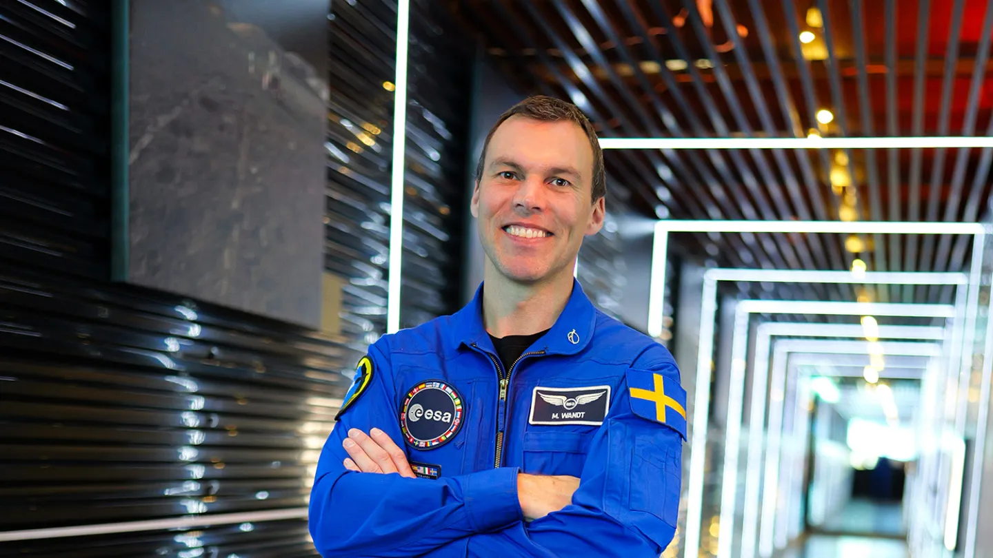 En manlig astronaut med korsade armar som ser glad ut.